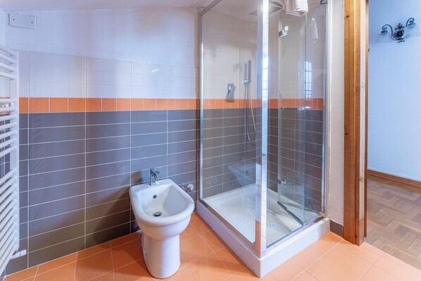A bathroom with a glass shower enclosure, a white pedestal sink, and a tiled floor with orange and gray tiles.