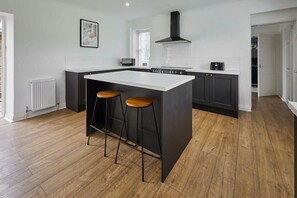 A modern kitchen with a central island, two stools, a stove, and a black range hood. - Host & Stay | Stay House (Northallerton)