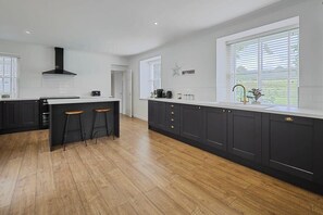 A modern kitchen with dark cabinetry, a central island with stools, and large windows providing natural light. - Host & Stay | Stay House (Northallerton)