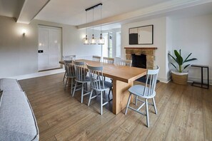 A modern kitchen with a wooden dining table, grey chairs, a built-in fireplace, and pendant lighting.