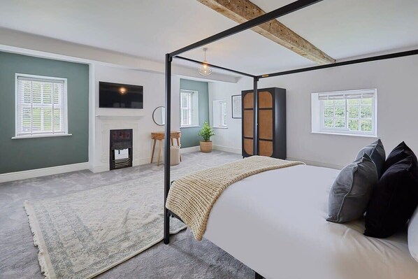 A bedroom with a four-poster bed, a fireplace, a large window, and a view of the outdoors.