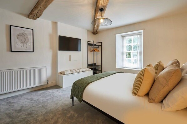 A bedroom with a bed, a radiator, a TV, a window, and a hanging light fixture.