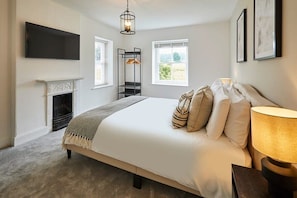 A bedroom with a large bed, a TV mounted on the wall, a fireplace, and a window with a view of greenery. - Host & Stay | Stay House (Northallerton)