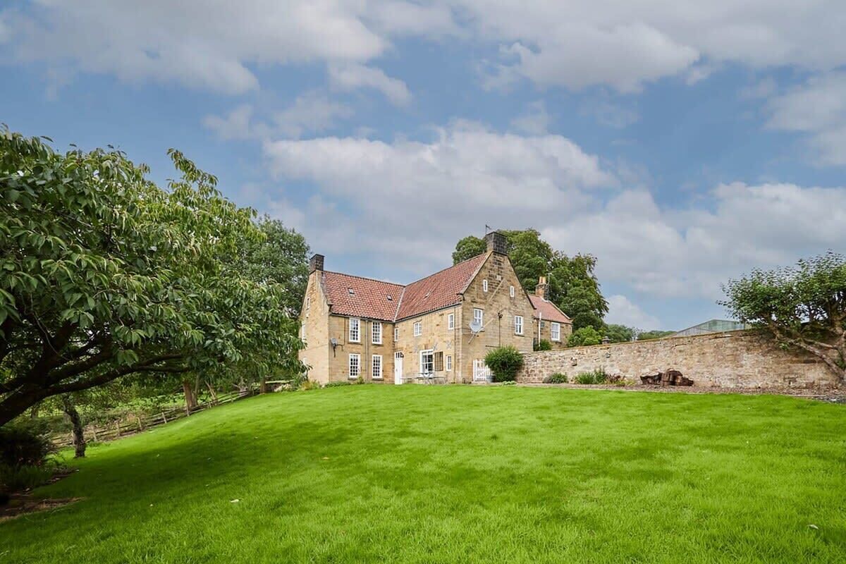 A stone building with a red-tiled roof, a grassy lawn, and a stone wall.