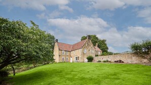 A stone building with a red-tiled roof, a grassy lawn, and a stone wall.