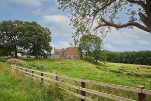 A rural house with a brick exterior, surrounded by lush greenery and a wooden fence.