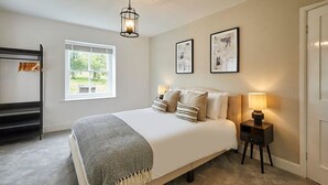 Une chambre à coucher avec un lit, des lampes de chevet, une fenêtre et un porte-vêtements suspendu.