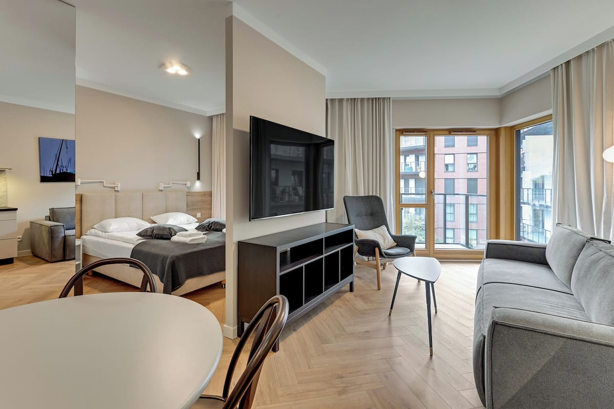 A modern hotel room with a bed, a sofa, a TV, and a dining area.