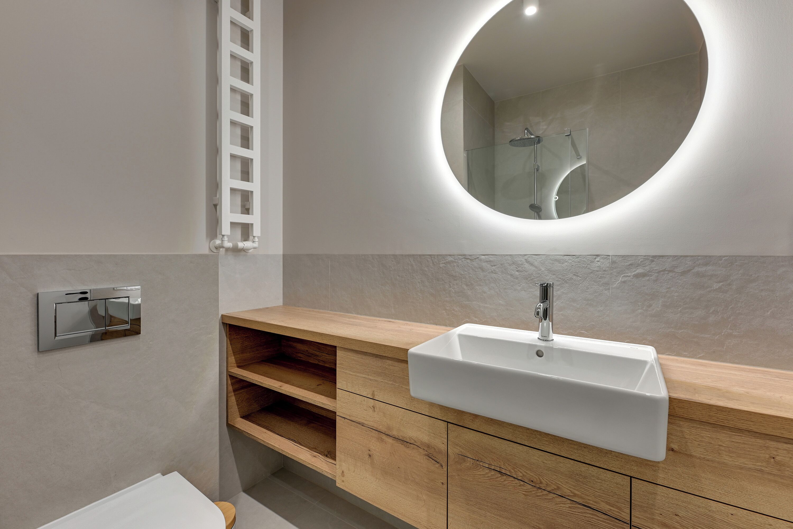 A modern bathroom with a white sink, wooden vanity, and a round mirror.
