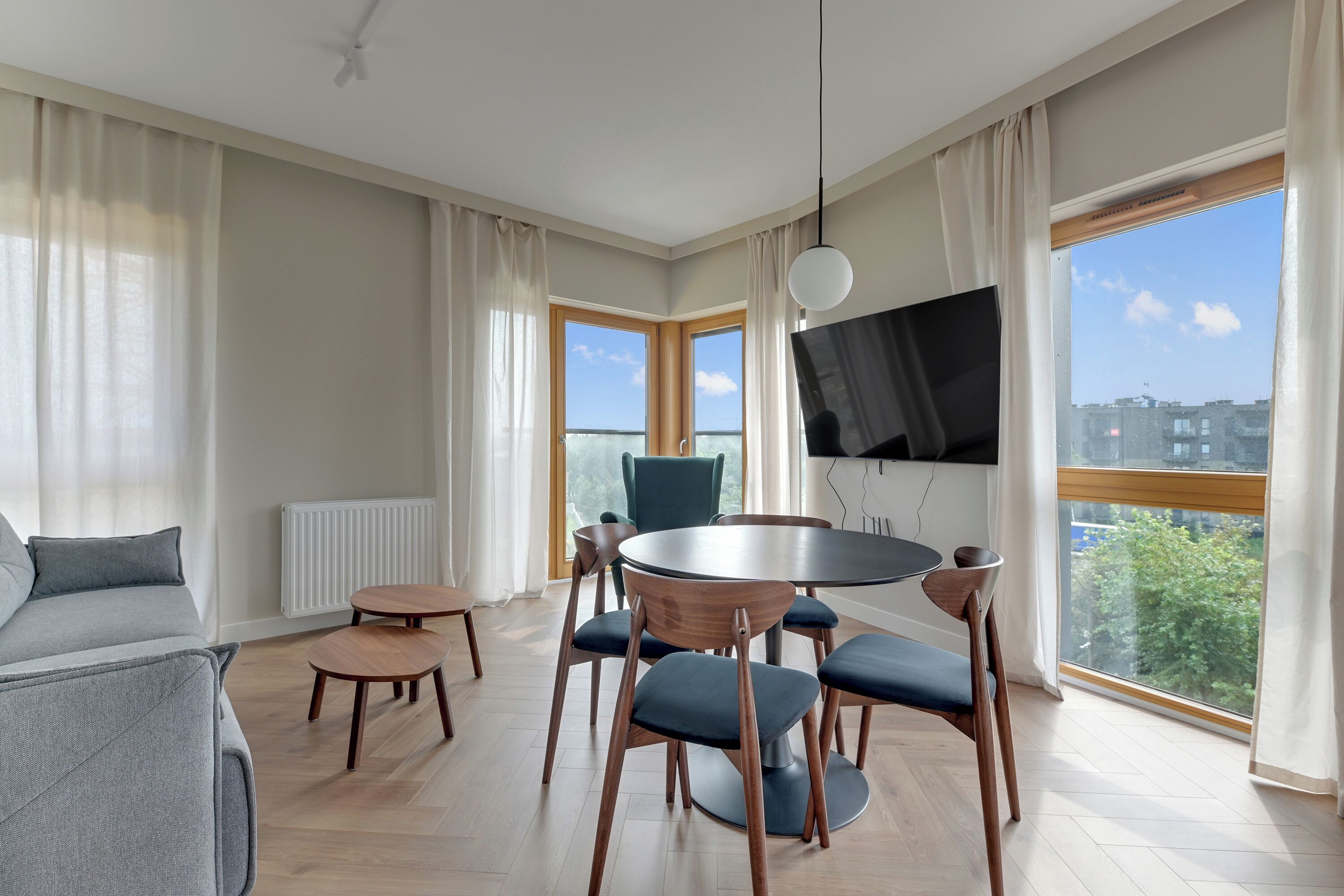 Ett modernt vardagsrum med ett runt matbord, blå stolar, en grå soffa och en tv som är monterad på väggen.