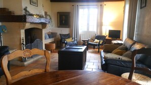 Un salon chaleureux avec une cheminée, un ensemble de canapés, une table à manger en bois et un téléviseur.