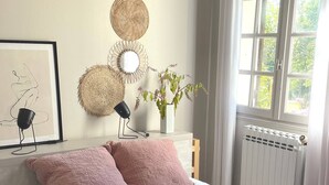 Un lit bien fait, avec une couette blanche et des oreillers roses, un plaid rouge et un vase rempli de fleurs posé sur une table de chevet.