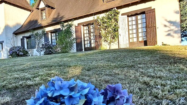 Une maison avec un toit en pente, de grandes fenêtres dotées de volets et une pelouse bien entretenue.