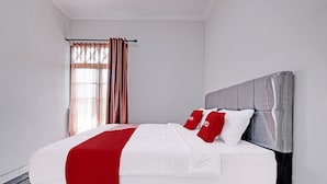 Una cama bien hecha con ropa de cama blanca y roja, un cabecero gris y una ventana con cortinas.