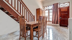 Un comedor con una mesa y sillas de madera, una escalera, un armario y una puerta con cortinas.