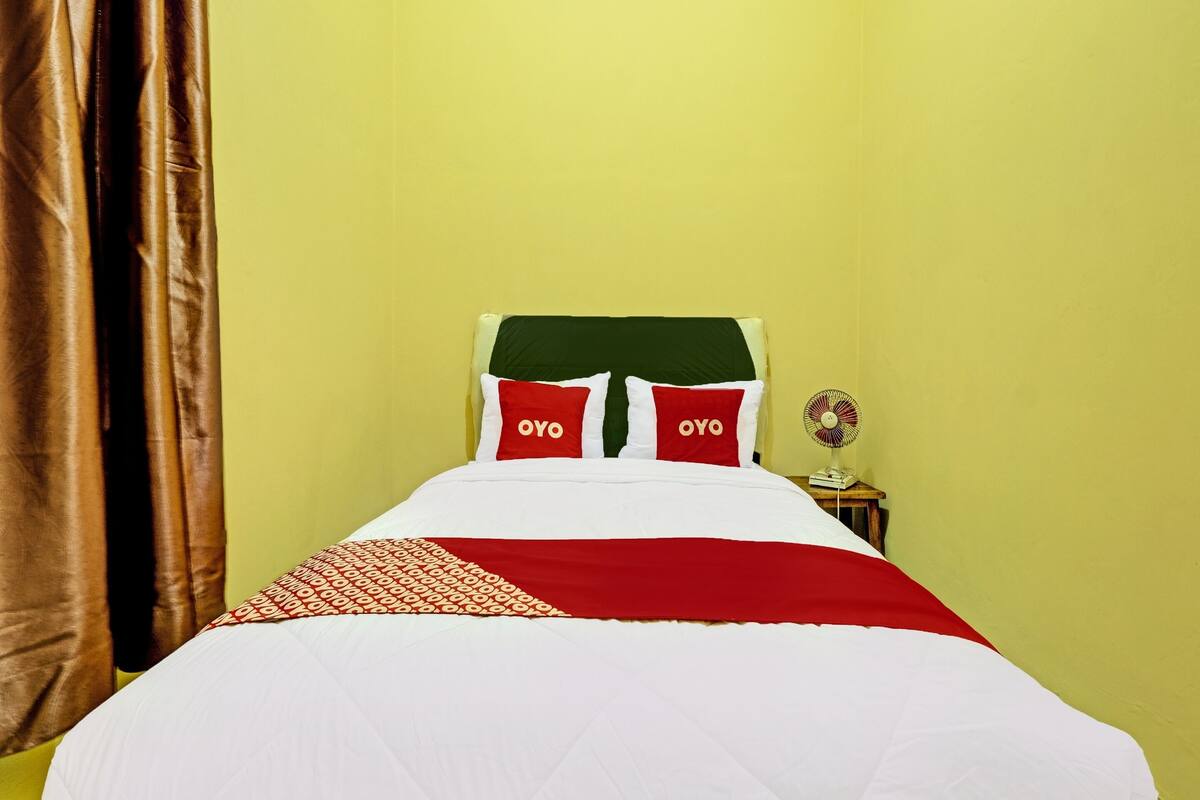 Ein Bett mit weißroter Bettdecke, zwei Kissen mit dem Schriftzug 'OYO' und ein Ventilator am Nachttisch.