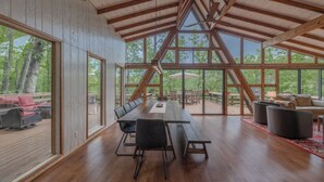 Un comedor amplio con una larga mesa de madera y bancos, ventanas grandes que ofrecen vistas al exterior, y una estructura de techo de madera.