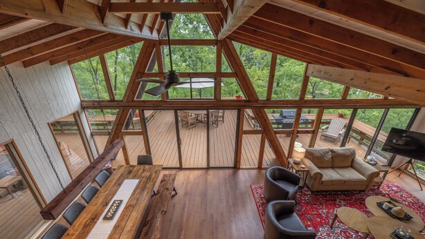 Un espacio amplio con una mesa de comedor de madera, un sofá y un televisor. Grandes ventanales ofrecen vistas al exterior.