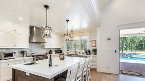Una cocina amplia con una isla grande, muebles blancos y vista a una piscina.
