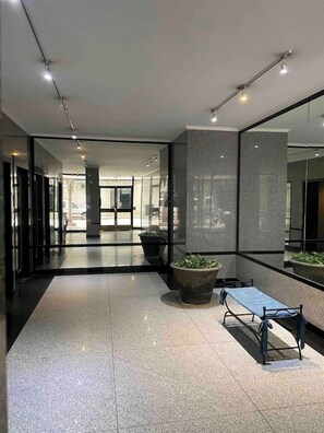 Eine moderne Lobby mit einer Bank, Topfpflanzen und einer Glaswand, die das Innere reflektiert.
