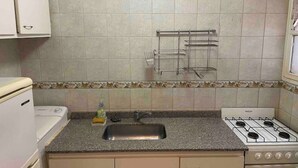 Une cuisine de taille réduite, équipée d’une cuisinière à gaz, d’un évier et de placards.