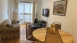 Un salon avec un canapé, une table de salle à manger ronde entourée de chaises, une guitare, un téléviseur et un tableau accroché au mur.