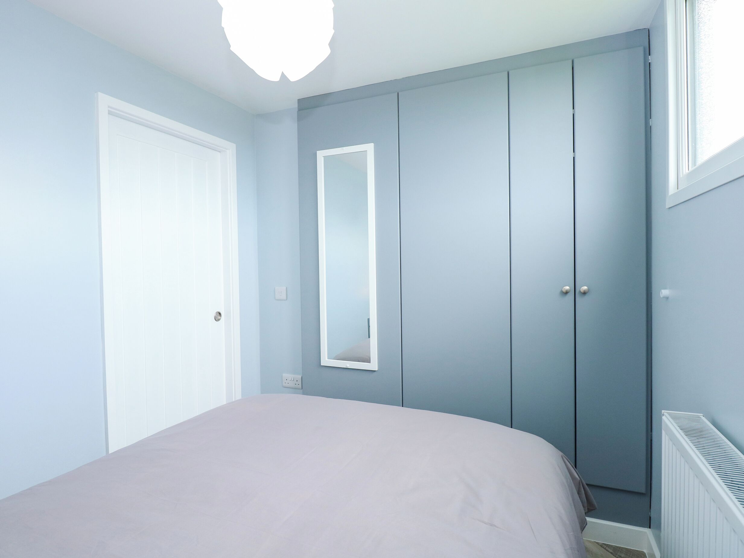 A bedroom with a bed, a wardrobe, a mirror, and a radiator.