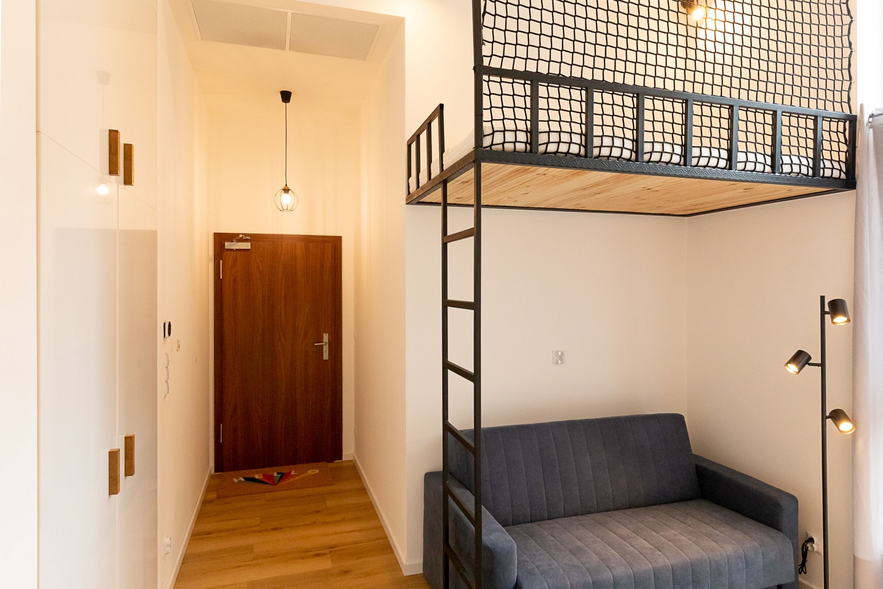 Una habitación con una cama individual encima de otra, un sofá, una puerta de madera y una lámpara.