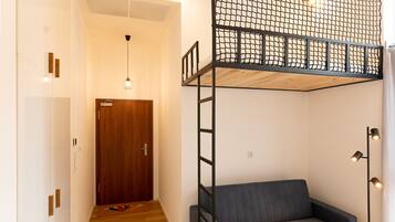 Una habitación con una cama individual encima de otra, un sofá, una puerta de madera y una lámpara.