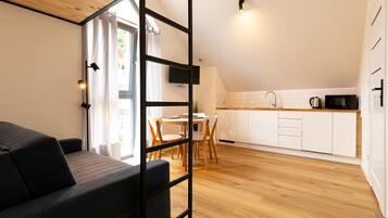 Una sala moderna con sofá, un comedor con mesa y sillas, y una cocina con armarios blancos y encimera de madera.