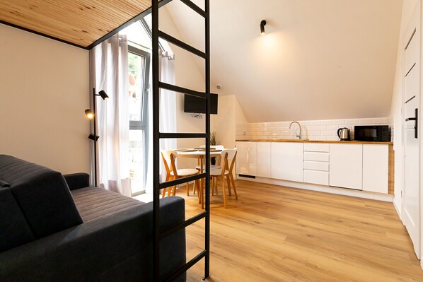 A modern living room with a sofa, a dining area with a table and chairs, and a kitchen with white cabinets and a wooden countertop. - RentPlanet - Kras Resort (Szklarska Poreba)