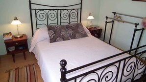 Ein Schlafzimmer mit einem Metallbettgestell, zwei Nachttischen mit Lampen, einem Bett mit gemusterten Kissen und einem gerahmten Bild an der Wand.