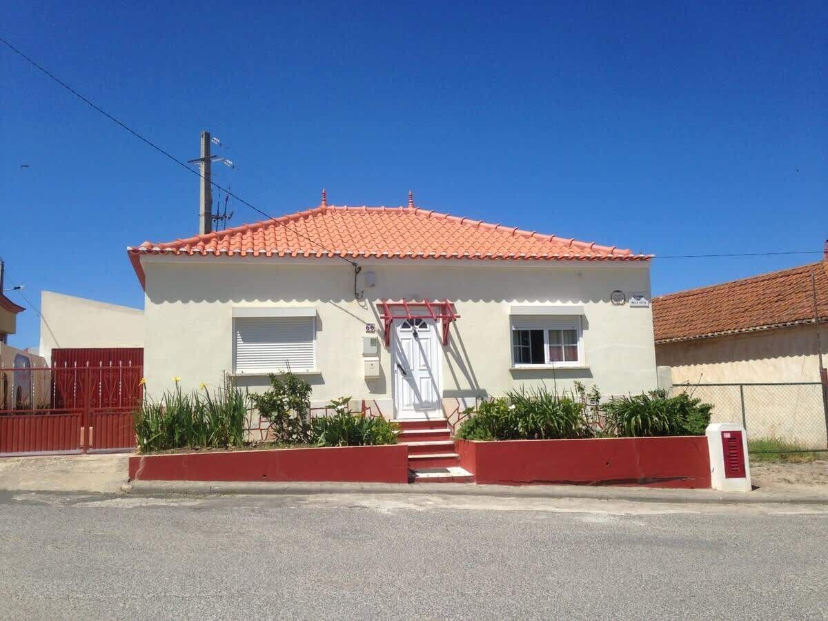 A two-story house with a red-tiled roof, a white exterior, and a red gate.