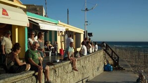 Ein Küstenweg mit sitzenden und stehenden Personen mit Blick auf den Strand.