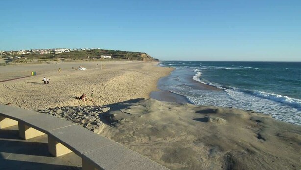 Ein Strand mit blauem Himmel, sandigem Ufer und einigen Personen.