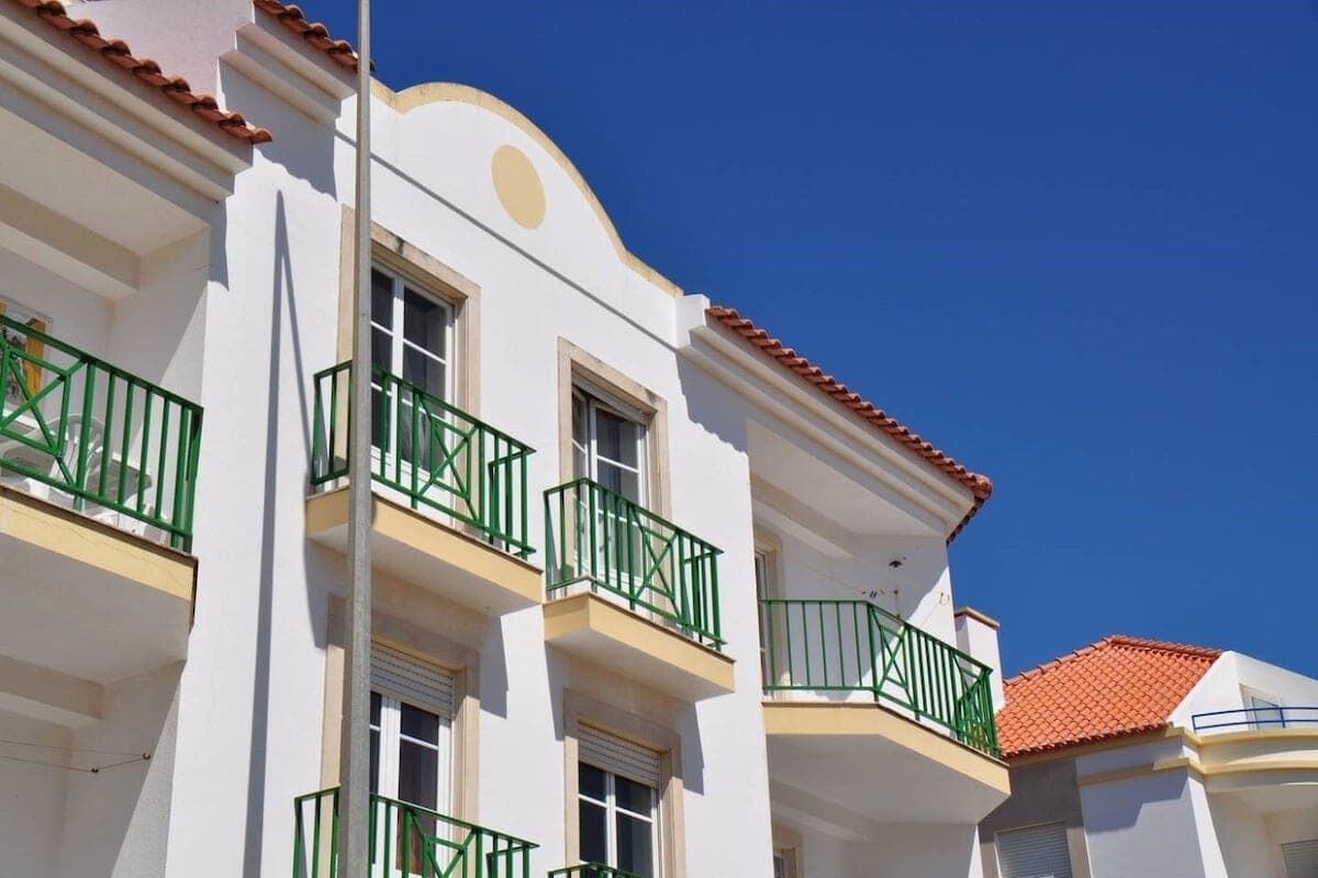 Un bâtiment blanc avec des balcons verts et un toit recouvert de tuiles rouges.