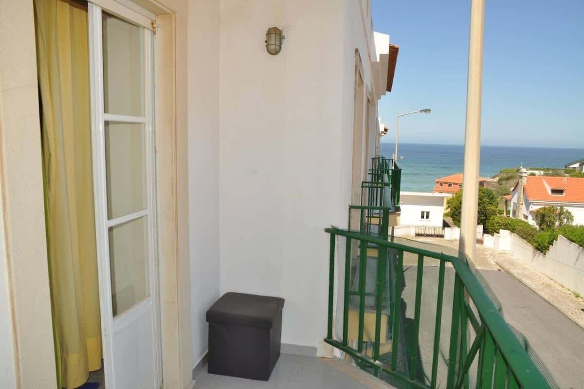 Un balcon avec vue sur la mer, une petite poubelle et une rambarde verte.