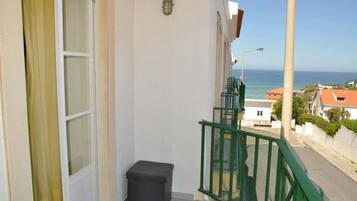 Un balcon avec vue sur la mer, une petite poubelle et une rambarde verte.