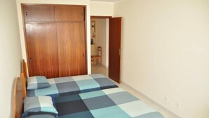 Ein Schlafzimmer mit einem Holzschrank, einem Bett mit karierter Bettdecke und einer Tür zu einem weiteren Zimmer.