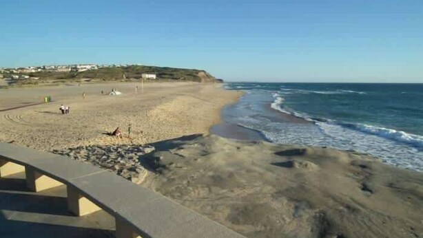 Ein Strand mit einer Betonpromenade, sandigem Ufer und Wellen.