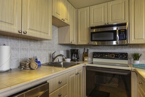 A kitchen with a stainless steel microwave, a built-in oven, a sink, and a coffee maker. - Kihei Surfside #102 1 Bedroom Condo by RedAwning (Kihei)