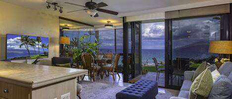 A spacious living area with a view of the ocean, a dining area with wicker furniture, and a kitchen with a bar.
