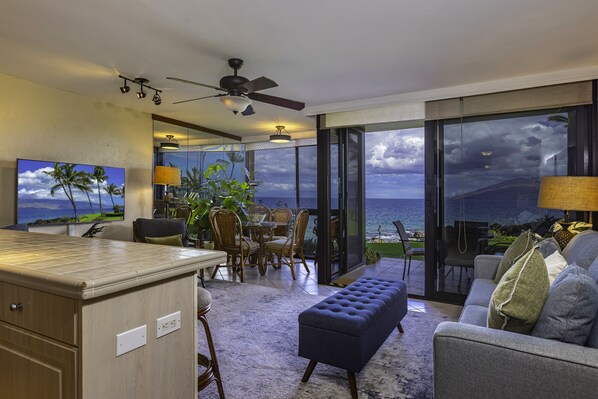 A spacious living area with a view of the ocean, a dining area with wicker furniture, and a kitchen with a bar.
