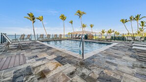 A pool area with lounge chairs and palm trees, overlooking a body of water.