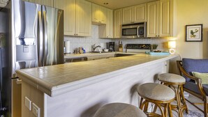 A modern kitchen with a stainless steel refrigerator, a built-in microwave, and a large island with bar stools.