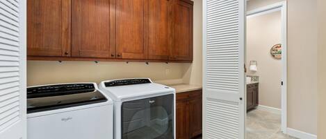 A laundry room with a Whirlpool washer and dryer, wooden cabinets, a white door, and a tiled floor.