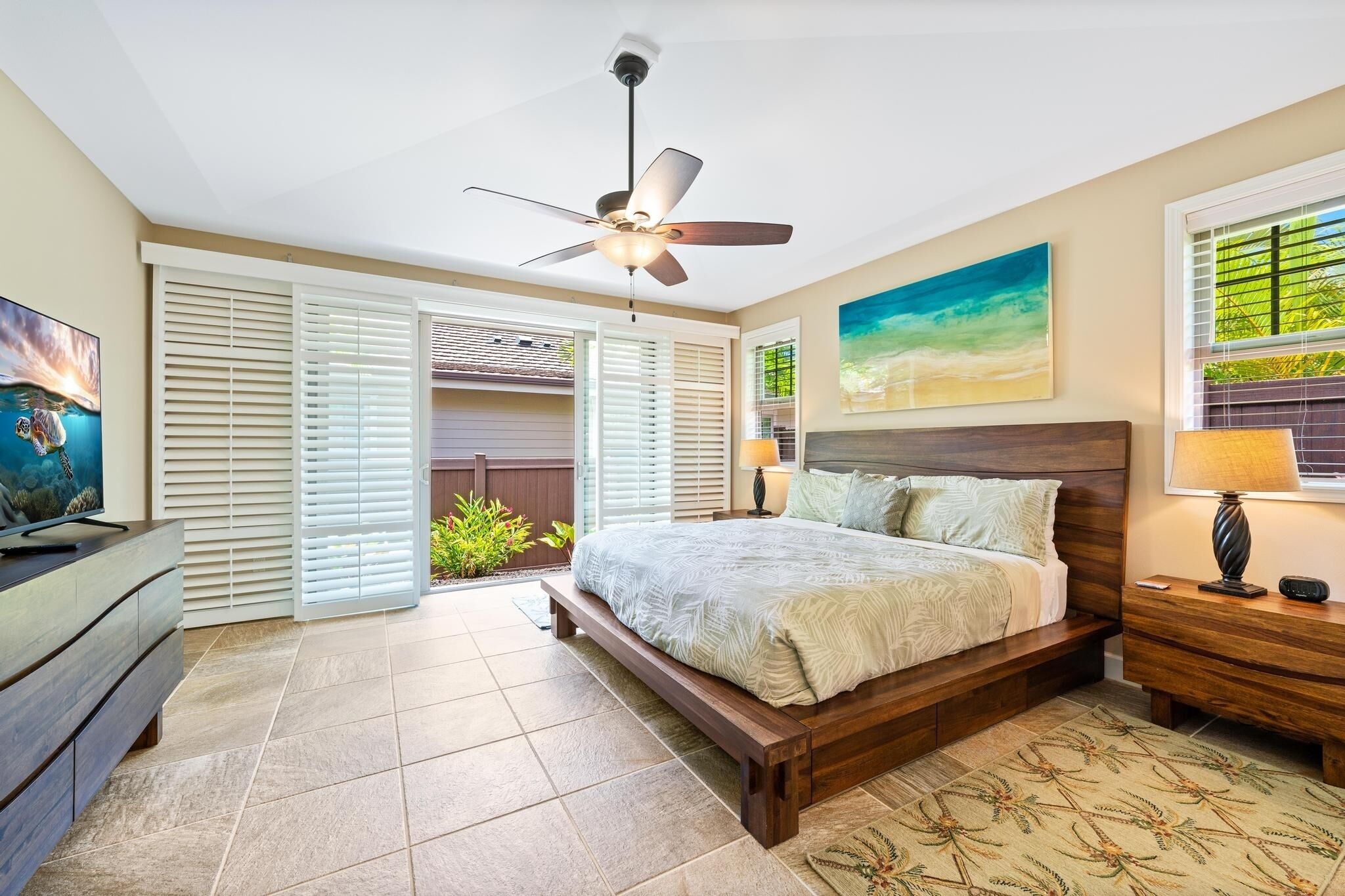 A bedroom with a bed, a ceiling fan, a TV, and a window with blinds.