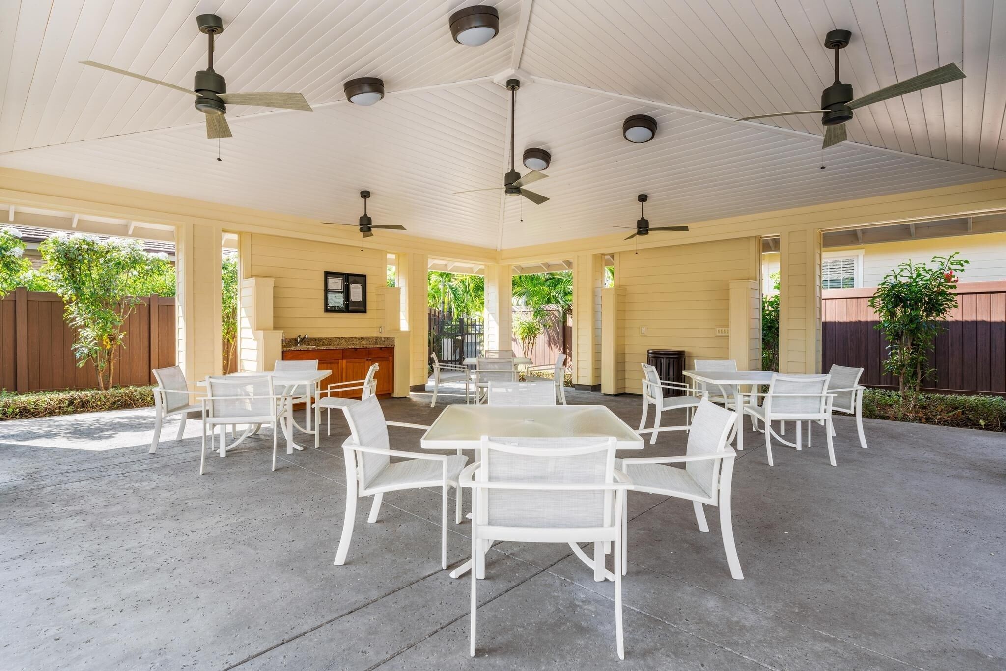 A covered outdoor patio with white tables and chairs, ceiling fans, and a view of the surrounding area.