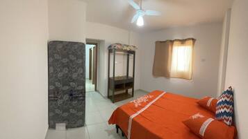A bedroom with a bed, a ceiling fan, a window with curtains, and a door leading to another room.