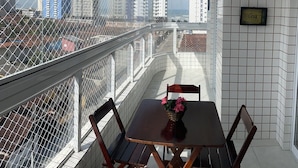 A balcony with a table and chairs, a potted plant, and a view of tall buildings. - Excelente Apto com piscina em Praia Grande (Praia Grande)